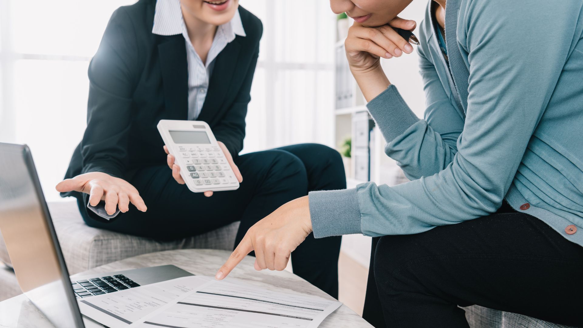 A financial advisor and property owner discuss landlord insurance policies, focusing on a document that likely outlines coverage specifics. They're engaged in a serious conversation over a laptop, indicating a comprehensive review of potential risks and insurance details to safeguard the owner's rental investment. The setting suggests a professional consultation to ensure the owner is well-informed about property damage coverage, loss of rental income, and liability protection as part of their investment strategy.