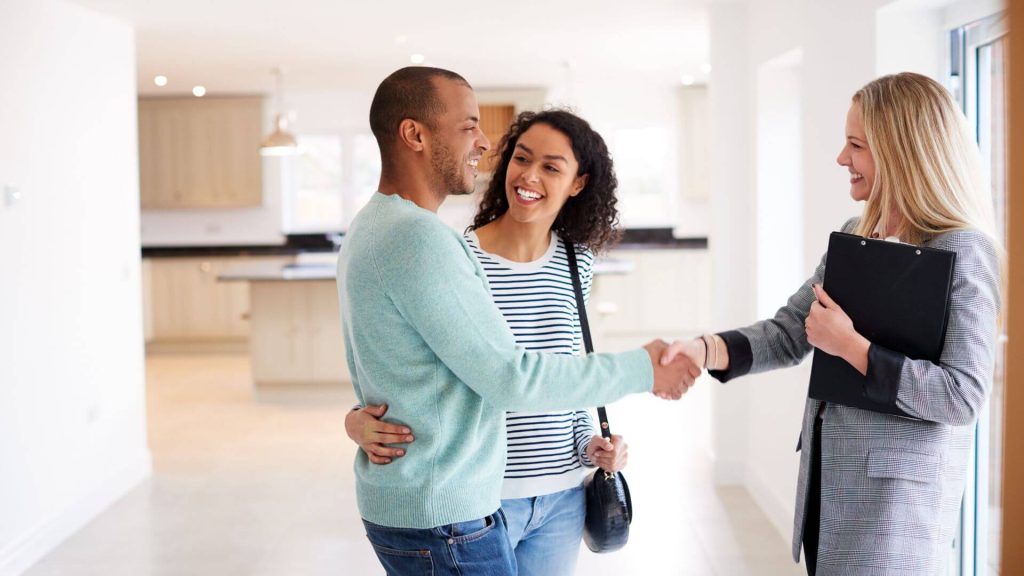 A smiling couple shake hands with a real estate agent inside a modern home, symbolising the successful process of buying a property.