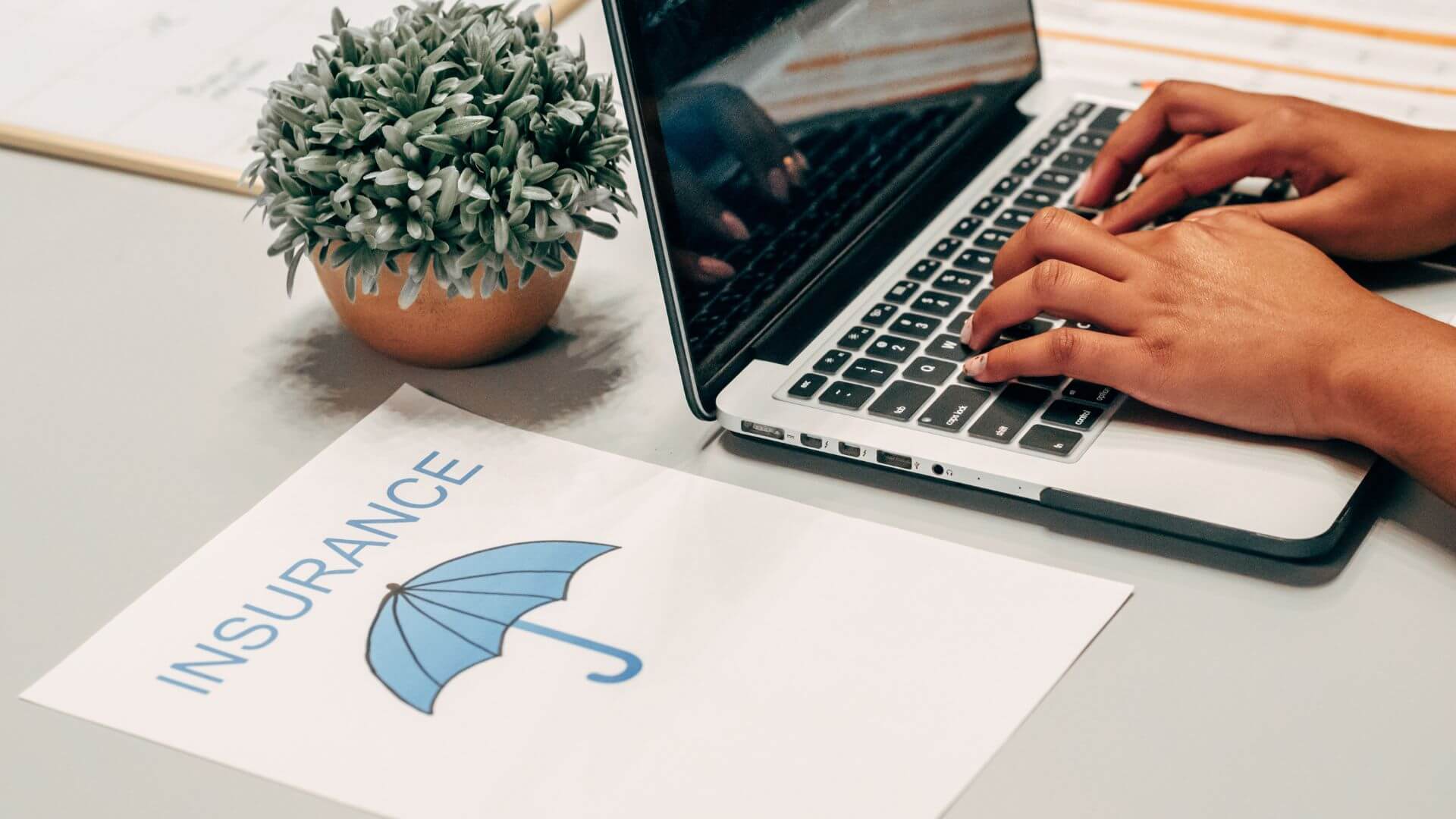 A person typing on a laptop next to a printed document labeled “Insurance” with an umbrella icon, representing research into indemnity insurance South Australia.